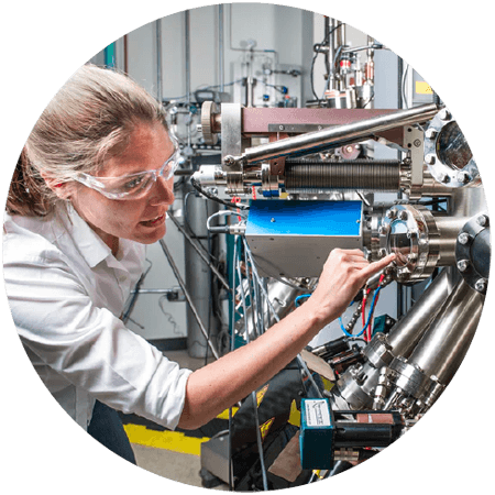 Woman wearing safety goggles pointing at machine