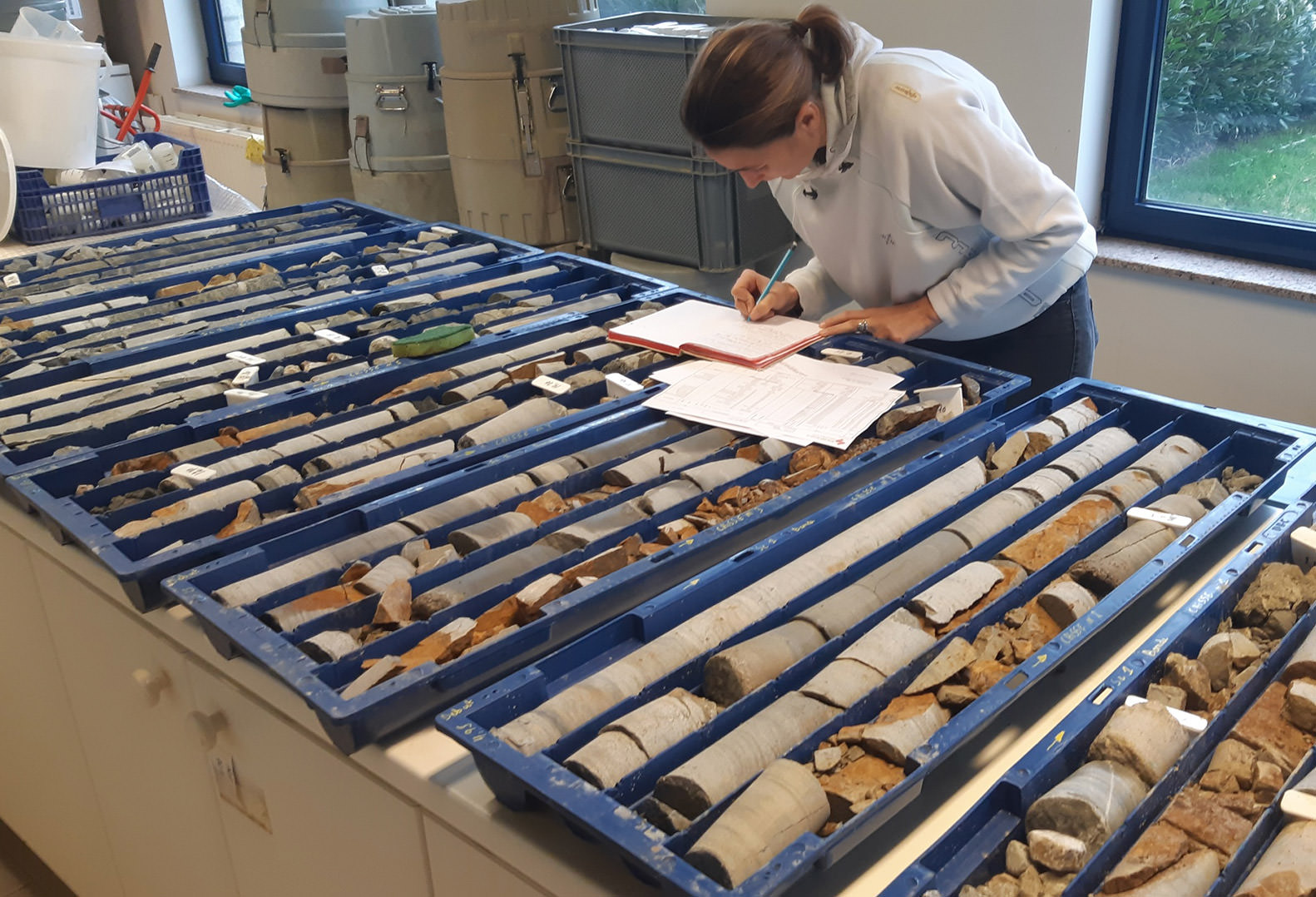 Woman wearing a white hoodie performs geological analysis in the AQUALE laboratory