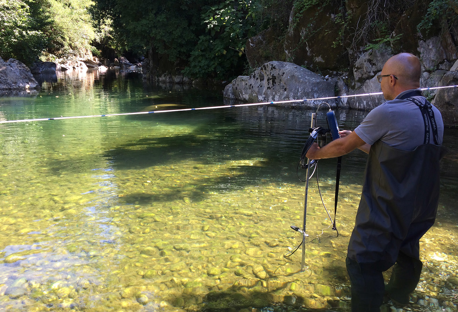 Man stands in creek and performs stream gauging and sampling